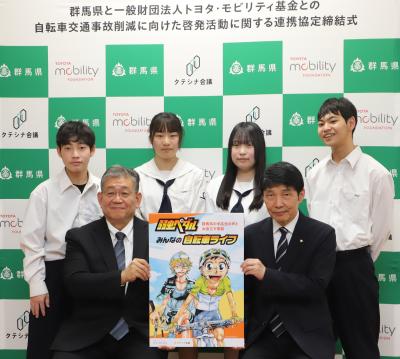 贈呈された『弱虫ペダル』冊子のパネルを掲げる山本知事と松田理事、伊勢崎清明高校生徒の写真